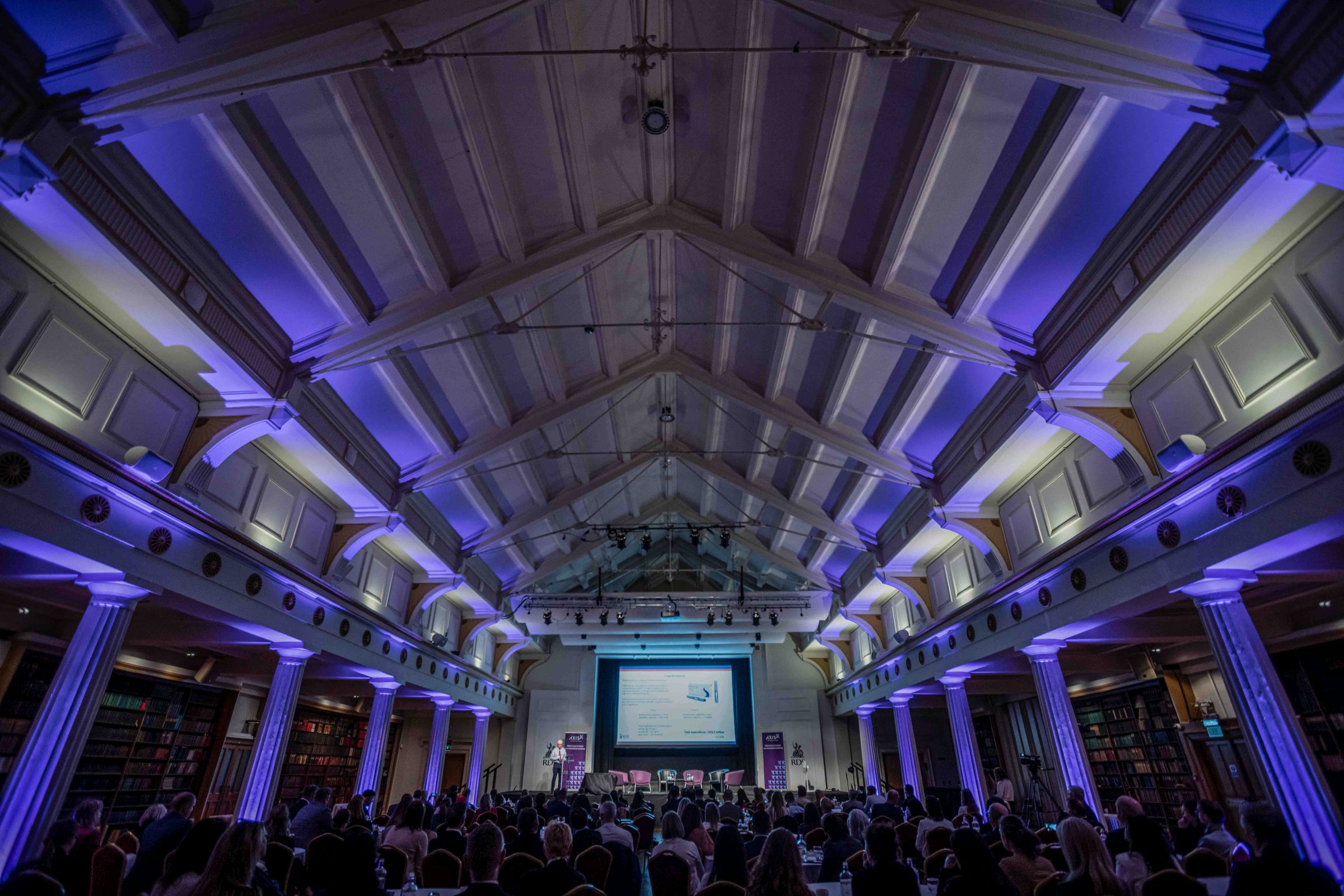 Sala główna konferencji z publicznością i sceną w fioletowym świetle